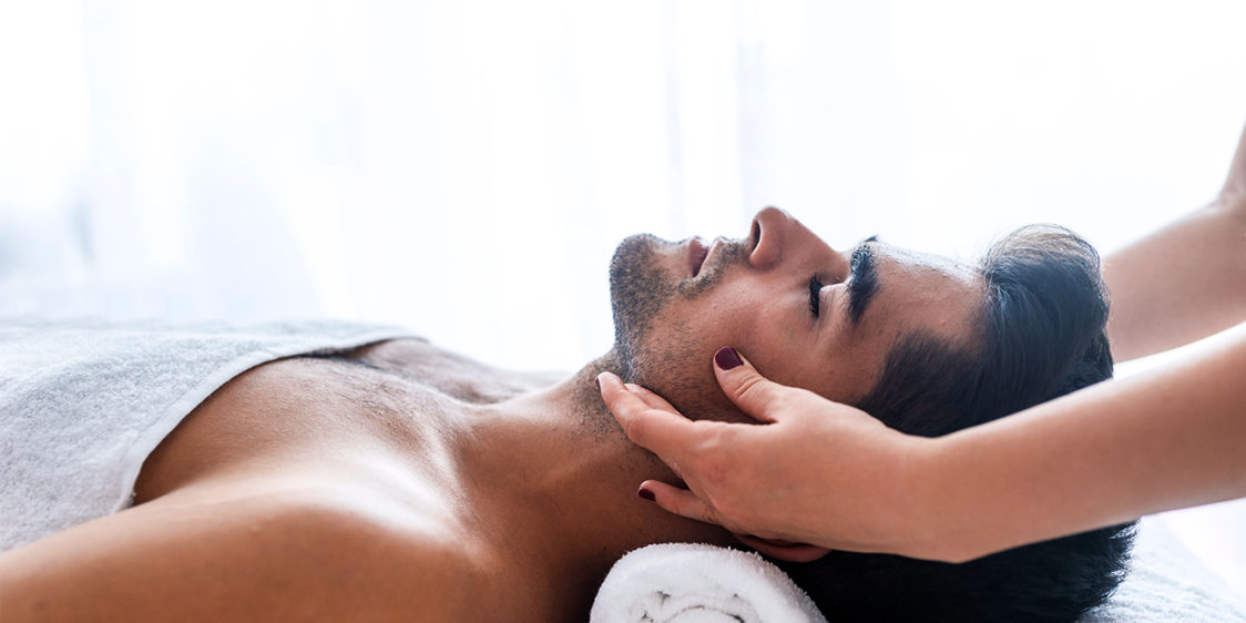 A spa therapist gives a facial to a male guest as part of male wellness practices.